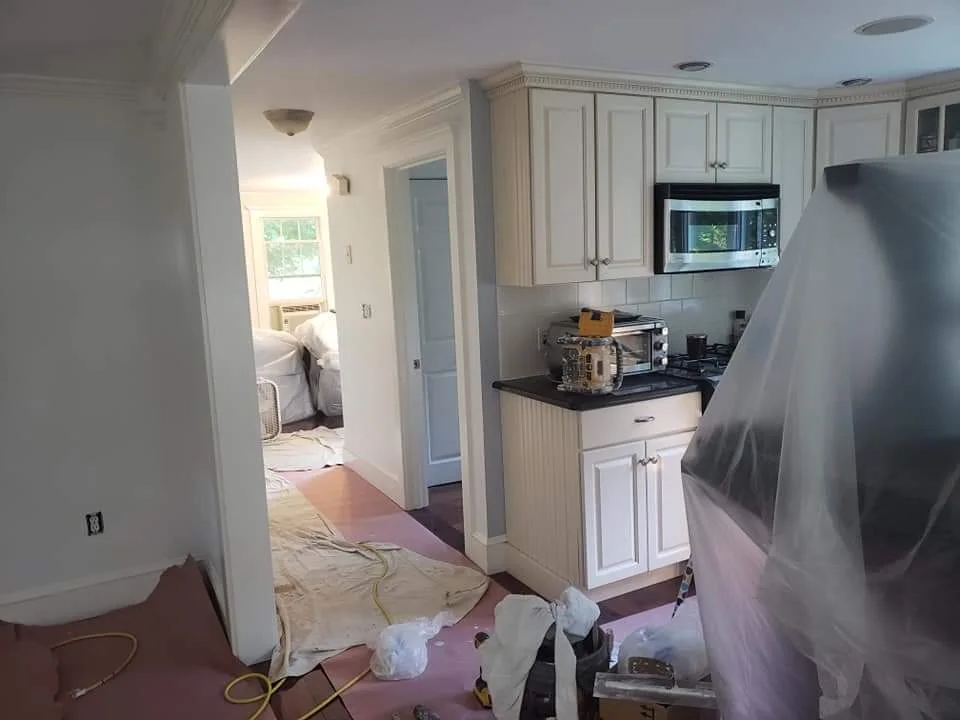 T&B Paint Pros LLC hallway off kitchen with soft blue paint, hardwood floors covered, kitchen island visible, Flagler County home interior painting.