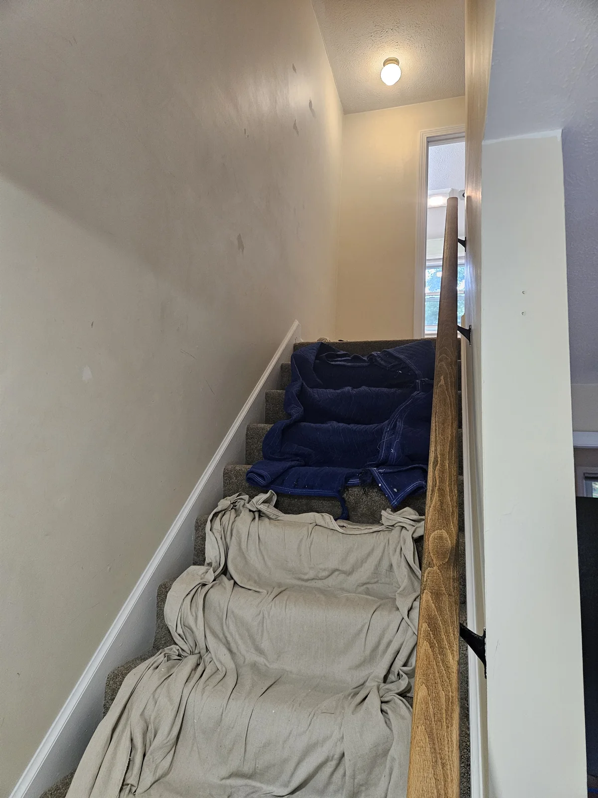 Before painting - hallway with dirty walls and covered stairs, showcasing the need for a fresh coat of paint. Flagler County Painter, Hallway Repainting, T&B Paint Pros LLC.