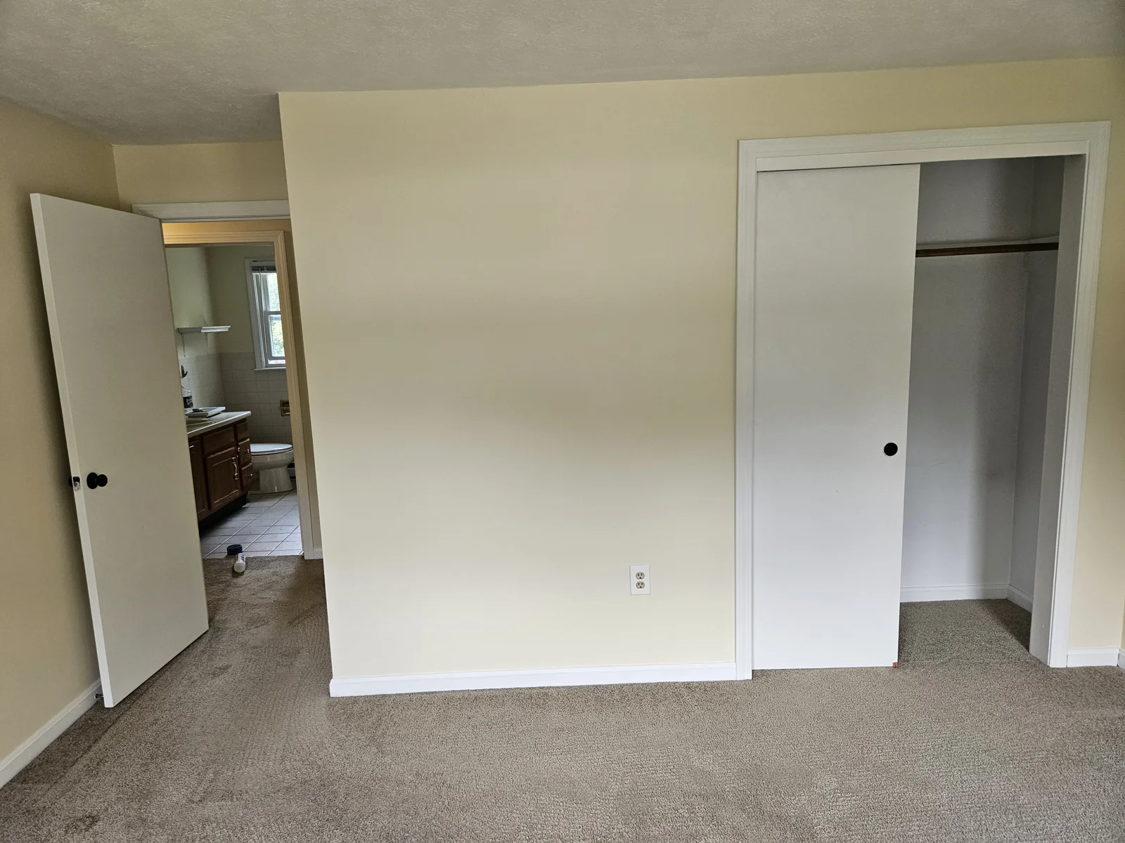 Inside the bedroom with soft yellow walls and newly painted doors. View of the open closet door and bedroom door. Flagler County Painter, Interior Painting, Bedroom Transformation, T&B Paint Pros LLC.