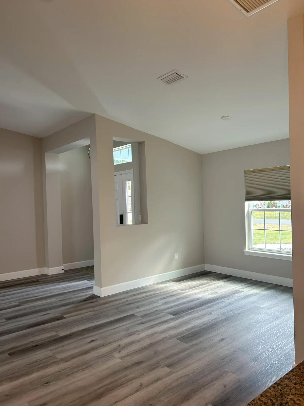 View from the kitchen looking toward the freshly painted entryway and dining nook in Palm Coast, FL. The walls are coated in Sherwin Williams Popular Gray with white trim, highlighting the open-concept design and vaulted ceilings.