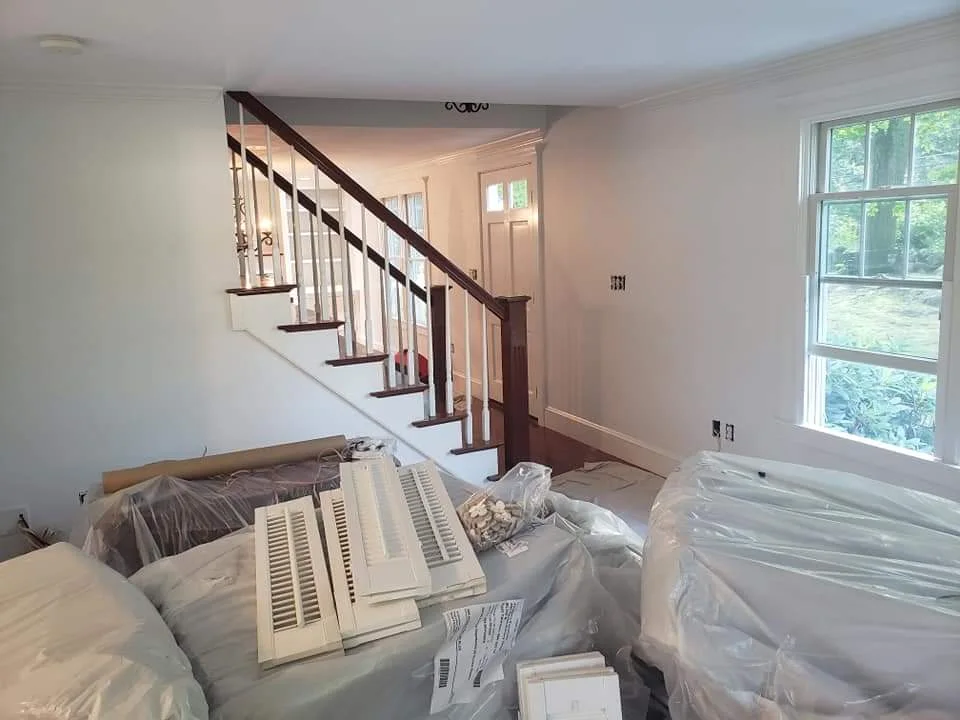 After: Entryway between dining and living room with freshly painted white walls, all belongings moved and covered for protection. The side view of the staircase is visible, showcasing a clean, bright transformation. Flagler County Painter, Residential Painting, Entryway Makeover, T&B Paint Pros LLC.