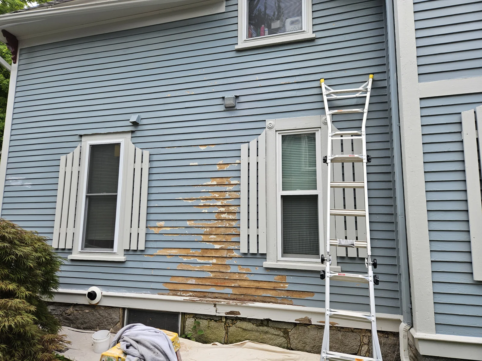 Exterior siding repair in progress—chipping paint removed and wood siding repaired on a soft blue home with white trim. T&B Paint Pros ensures a flawless foundation for repainting. tbpaintpros Flagler County Florida experienced painter for expert home restoration and painting services.