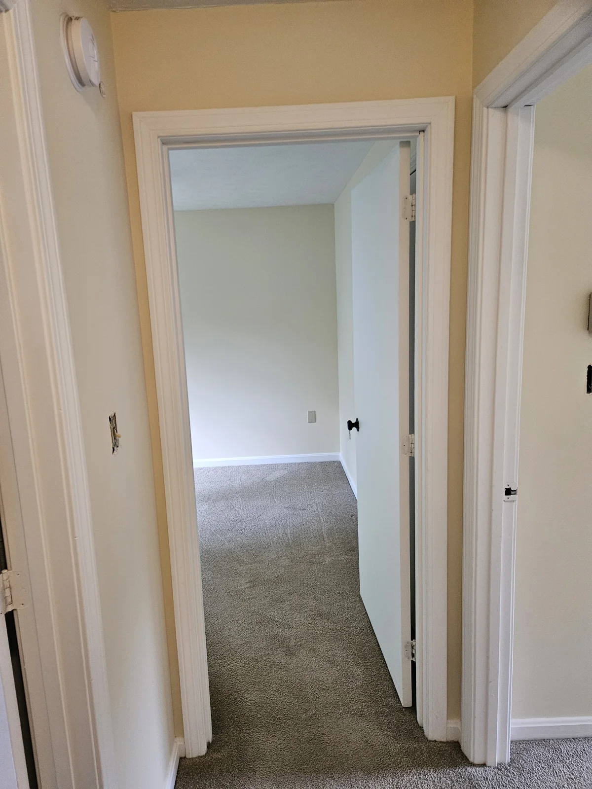 Hallway with freshly painted walls leading into the bedroom. The soft yellow bedroom walls are visible in the background, offering a smooth transition and brightened space. Flagler County Painter, Interior Painting, Hallway and Bedroom Transformation, T&B Paint Pros LLC.